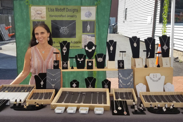 Lisa Medoff smiling by green banner and jewelry stand
